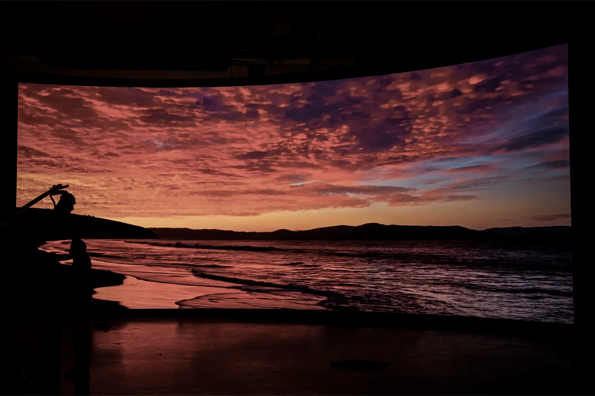 Camera rig silhouetted against a sunset coastline on the LED wall